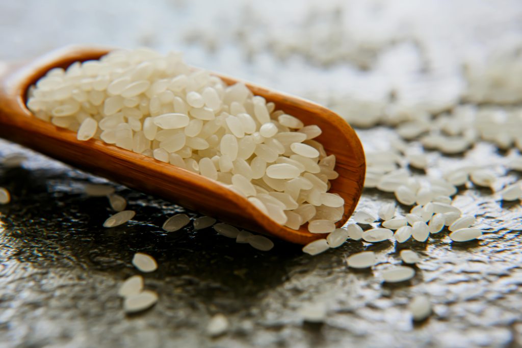 Detailed close-up of uncooked rice grains spilling from a wooden spoon on a textured surface.